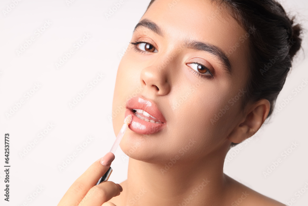 Young woman applying lipgloss on light background, closeup