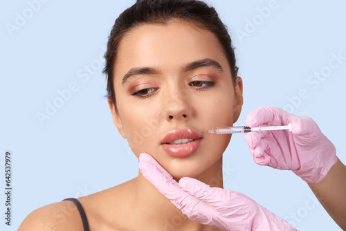 Young woman receiving lip injection on blue background  closeup