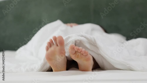 Woman stretches while lying in kingsize bed after good healthy sleep. Close up of feet. Morning awakening photo