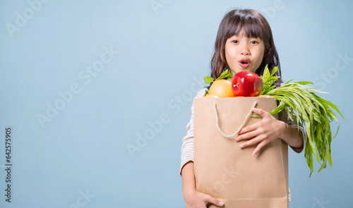 A little girl is holding a paper bag with mixed vegetables and fruits.