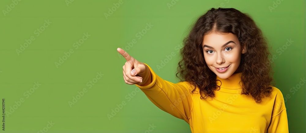 Teenage girl with finger pointing happy with copy space green paper yellow background Teenage girl with finger pointing happy with copy space green paper yellow background