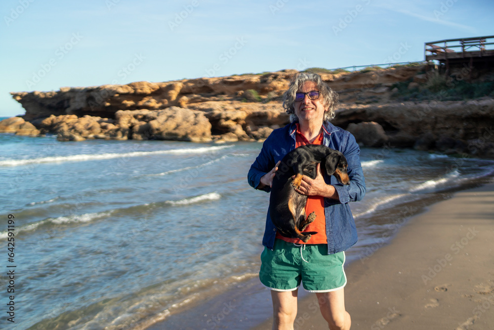A fifty-year-old man enjoying with his Dachshund in his arms at the beach