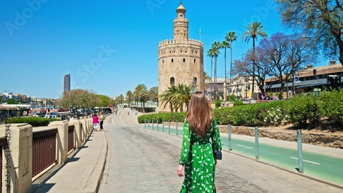 Tourist girl in a dress walking towards Torre del Oro Fortress in Seville, Spain. A female woman looking at the Spanish Old defensive military watchtower in Seville, Europe