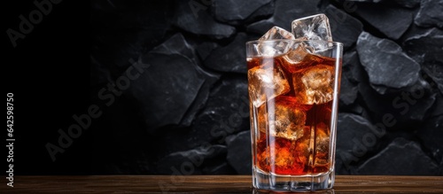 Cola filled glass on a dark rustic surface with ice