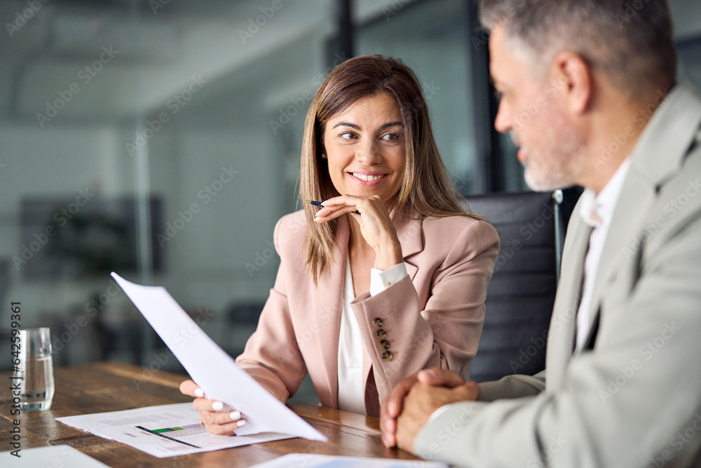 Two business executives discussing financial legal papers in office at meeting. Smiling female lawyer adviser consulting mid aged client at meeting. Mature colleagues doing project paperwork overview. - obrazy, fototapety, plakaty 