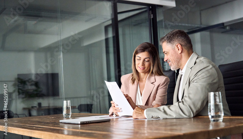Two professional executives discussing financial accounting papers working with paperwork in office. Mature business woman and man managers holding legal corporate documents at meeting. Copy space.
