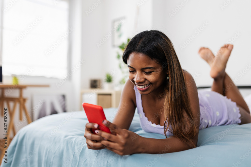 Young latin teen student girl using smartphone while relaxing on bed at home. Millennial female chatting on cellphone through social media app Young latin teen student girl using smartphone while relaxing on bed at home. Millennial female chatting on cellphone through social media app