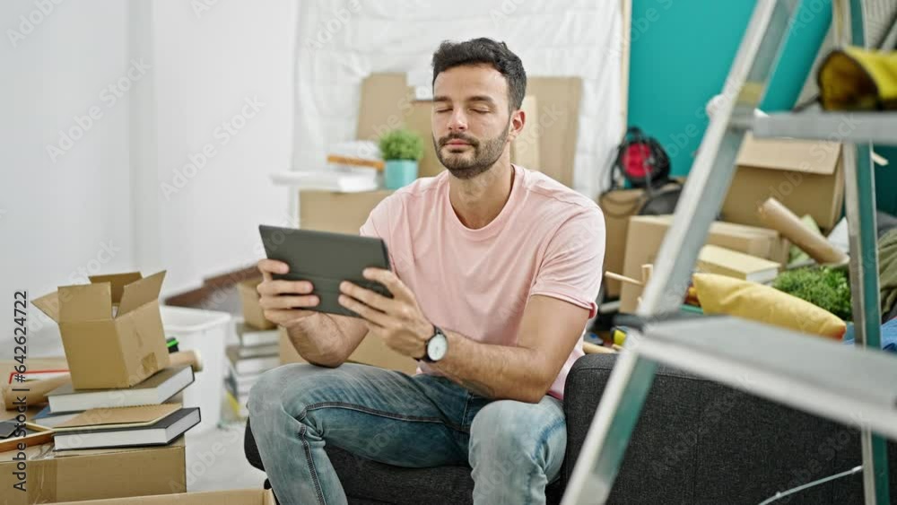 Young hispanic man using touchpad sitting on sofa at new home Young hispanic man using touchpad sitting on sofa at new home