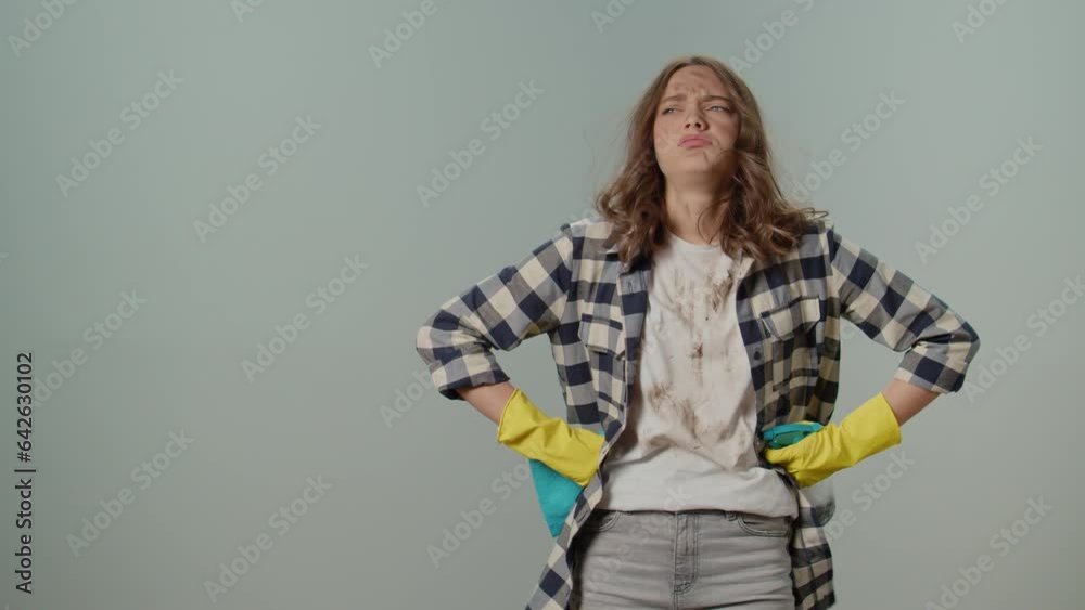 Dirty Upset Angry Young Woman Housewife In Yellow Gloves Holding a Cleaning Spray Bottle and Rag, Keeps Her Hands on Her Sides on the Gray Background. Cleaning for Appliance Efficiency and Iongevity. Dirty Upset Angry Young Woman Housewife In Yellow Gloves Holding a Cleaning Spray Bottle and Rag, Keeps Her Hands on Her Sides on the Gray Background. Cleaning for Appliance Efficiency and Iongevity.
