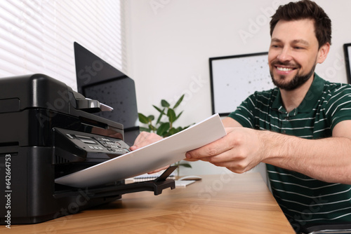 Man using modern printer at wooden table indoors, selective focus