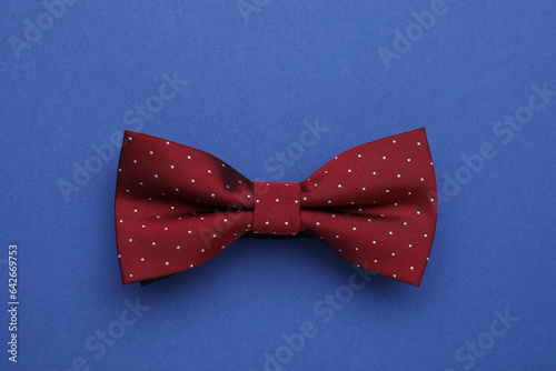 Stylish burgundy bow tie with polka dot pattern on blue background, top view