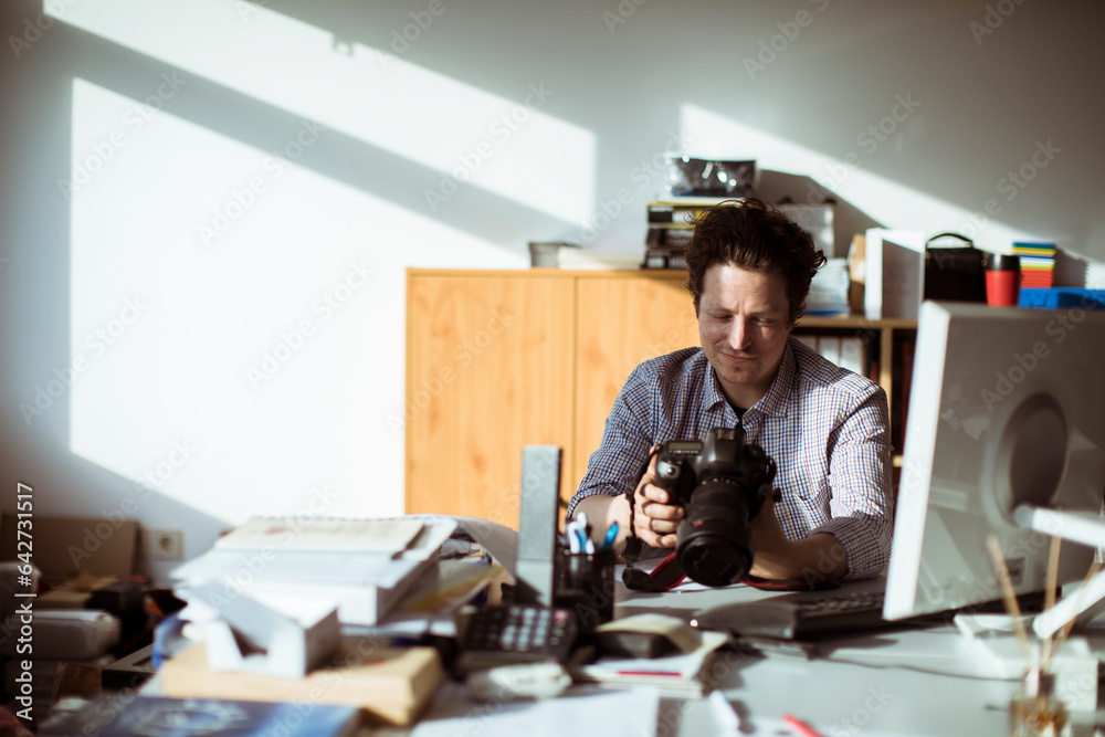 Young photographer going through his camera at his desk office Young photographer going through his camera at his desk office
