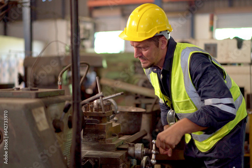 Professional caucasian white ethnicity male technician operating the heavy duty machine in the lathing factory. Technician in safety and helmet suit controlling a machine in factory. © DG PhotoStock