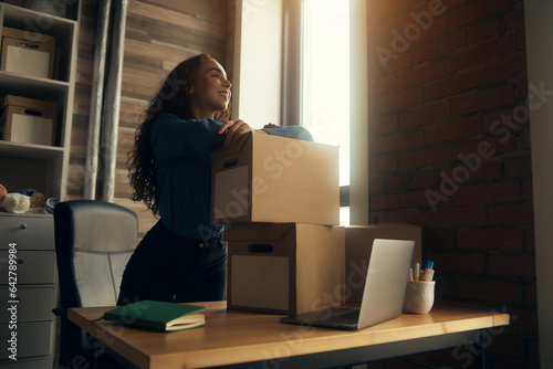 A young curly-haired logistics employee packs goods, collects parcels, puts things in a cardboard box, prepares a parcel for shipment, transports, sits on a windowsill and drinks a report in a book © Alexandr
