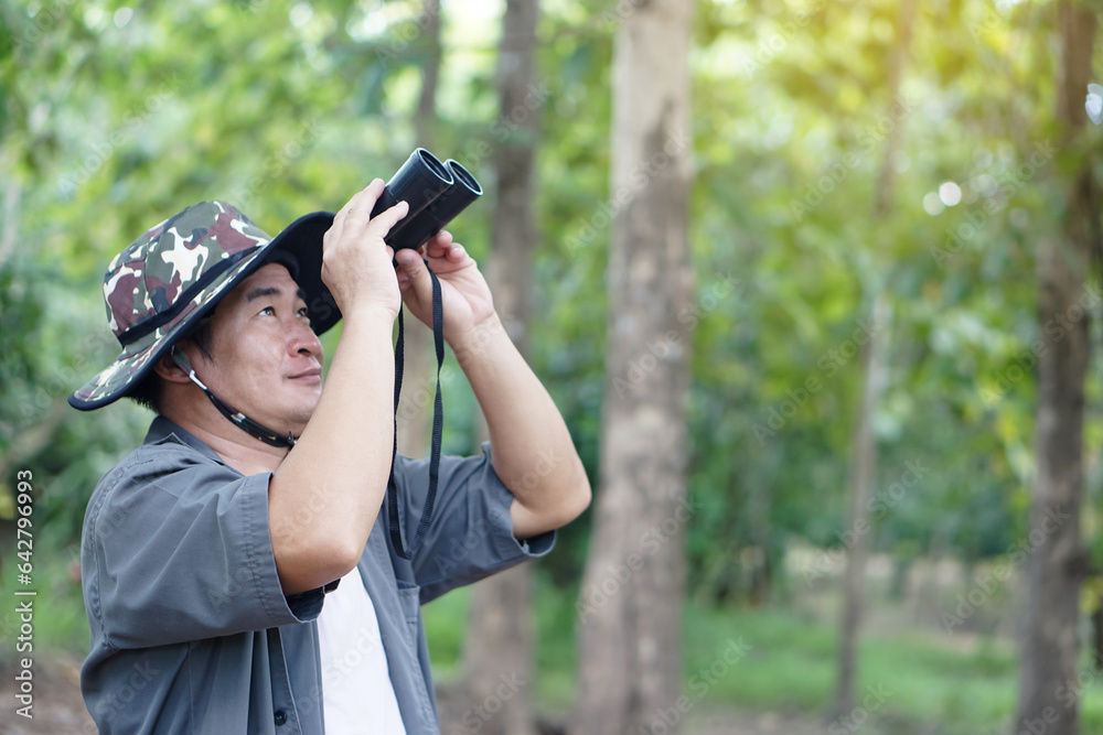 Asian man ecologist use binocular to survey nature in forest. Concept, nature exploration. Ecology study. Pastime activity, lifestyle. Explore environment. Traveling alone Asian man ecologist use binocular to survey nature in forest. Concept, nature exploration. Ecology study. Pastime activity, lifestyle. Explore environment. Traveling alone