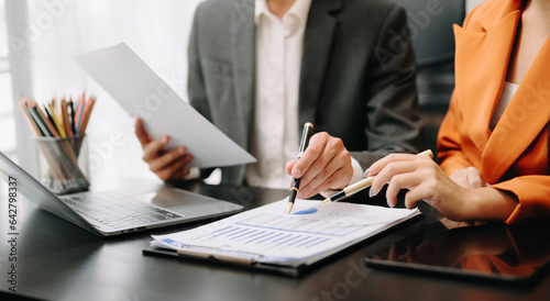 Business documents on office table with smart phone and calculator digital tablet and graph business with social network diagram and two colleagues discussing data working in the office..