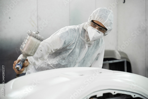 Automotive service worker in full protective gear expertly apply color paint in to car\'s bodywork with spray gun or respirator painting in chamber workshop. Car paint service for scratch refinish.Oxus