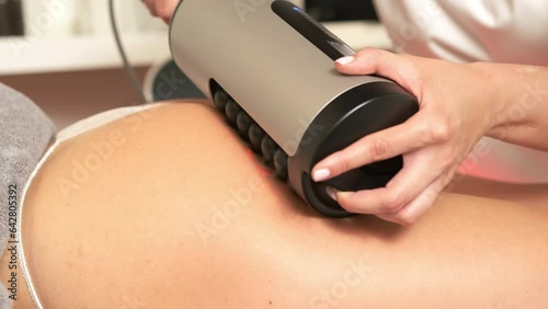 Modern electric massager with usage to correct body shape in clinic. Professional massage master works with clients legs with vibrotherapy machine photo