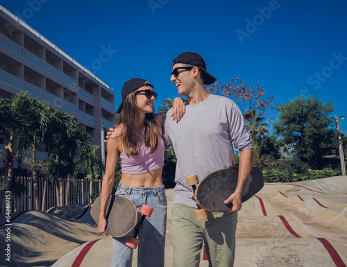 Young happy couple with skateboards enjoy longboarding at the skatepark photo