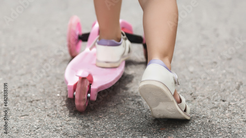 Child riding scooter. Happy little kid girl playing pink kick board on road in park outdoors on summer day, Active children games outside, Kids sport healthy lifestyle concept