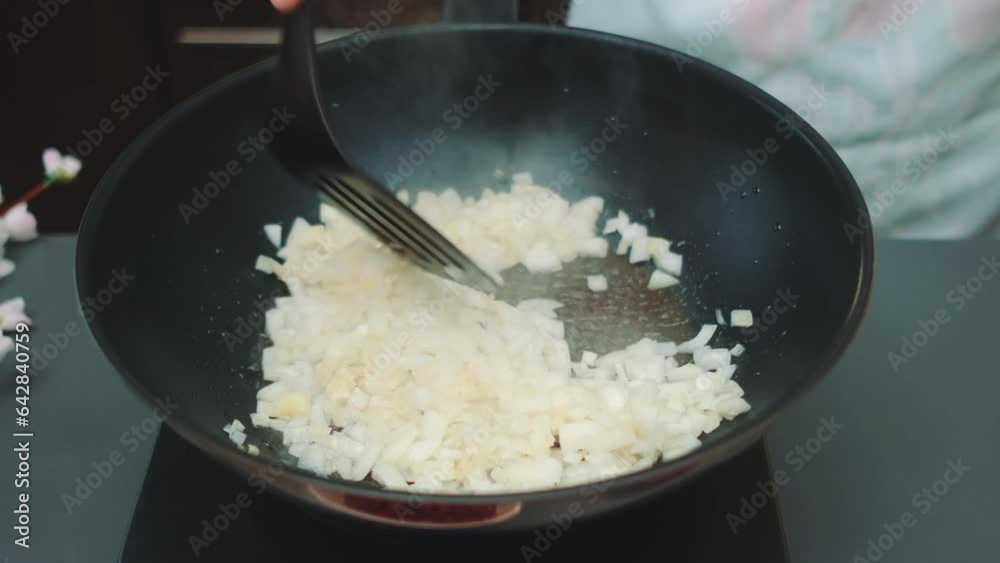 Woman cook frying onions in a deep wok frying pan stirring frequently. Middle shot of table. Cooking in the kitchen