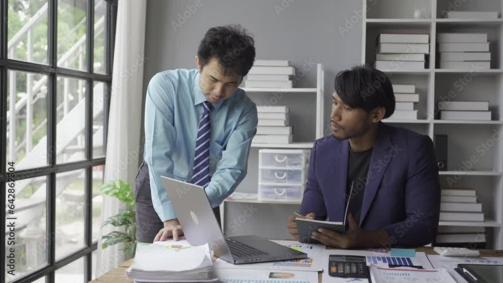 Two young asian businessmen in suits discussing financial market data in office Business team working with charts Stock traders analyze statistics Dynamics shown on graphs Two young asian businessmen in suits discussing financial market data in office Business team working with charts Stock traders analyze statistics Dynamics shown on graphs