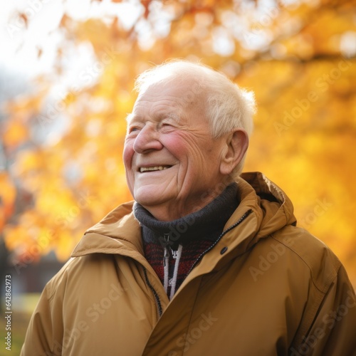 An elderly man wearing a brown parka is smiling amongst the vibrant orange and brown autumn leaves, celebrating the beauty of nature in the crisp months of september, october, and november © mockupzord