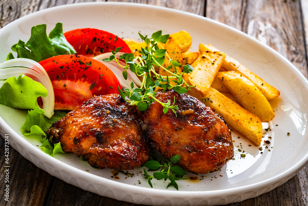 Roasted chicken thighs with French fries and fresh vegetables on wooden table
Roasted chicken thighs with French fries and fresh vegetables on wooden table