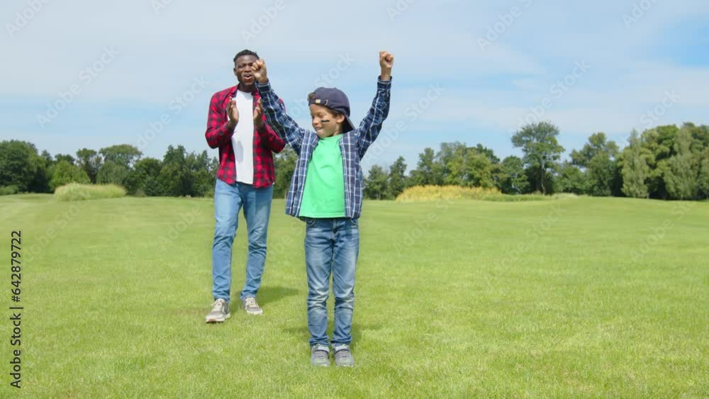 Excited preadolescent African American son with joyful black father celebrating touchdown with winning gesture on field , expressing joy and happiness while family playing American football game. Excited preadolescent African American son with joyful black father celebrating touchdown with winning gesture on field , expressing joy and happiness while family playing American football game.