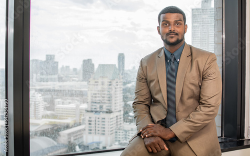 Obraz na plátne Portrait of handsome African smart business man wearing formal suit and necktie, smiling with confidence, success and looking at camera with copy space, sitting beside window in indoor office
