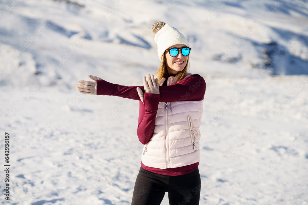 Happy woman in warm clothes exercising arm on snowy plain