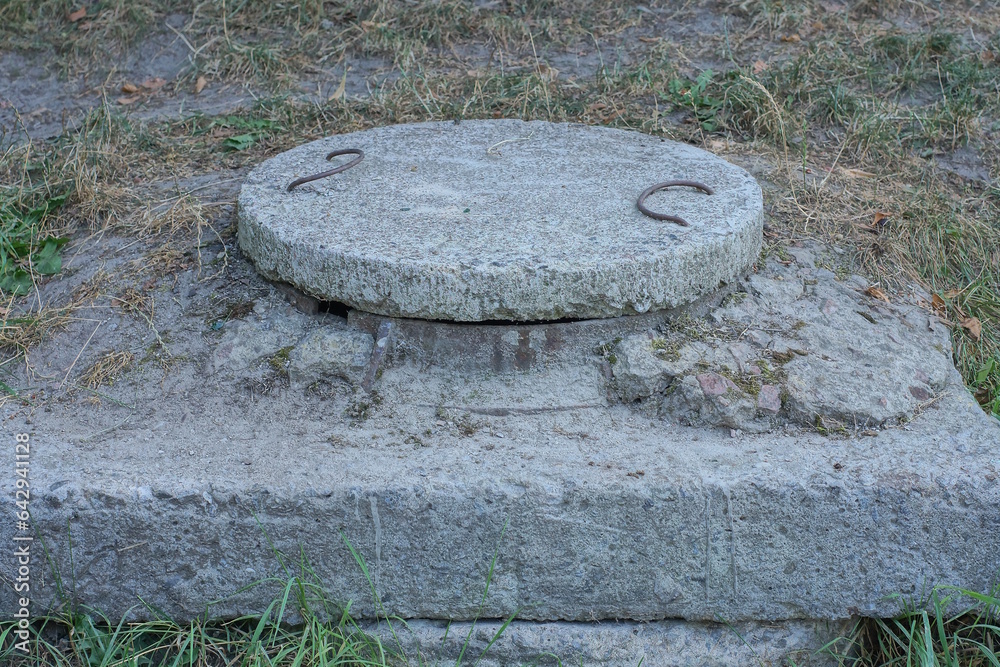 one large gray concrete manhole on the street in the green grass