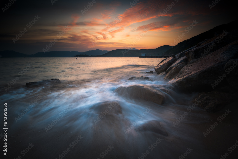 sunset over the sea with water flow and rock in foreground
