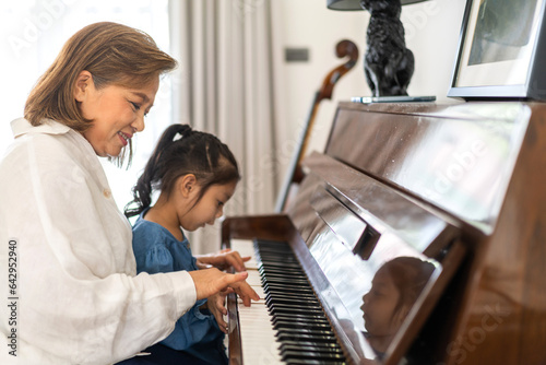 Portrait of happy love asian grandmother and asian cute girl play and enjoy relax teaching and play piano music lesson at home.senior, insurance, care.girl with their laughing grandparents.Family