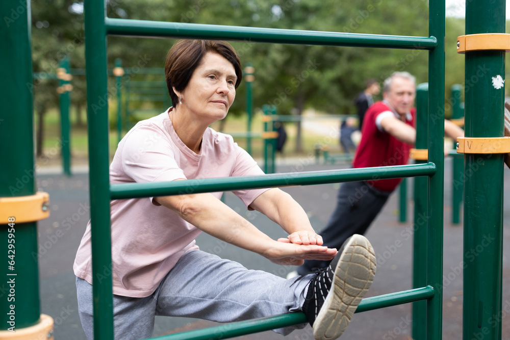 Φωτογραφία Elderly woman is engaged in stretching on sports bars on an open-air sports fiel