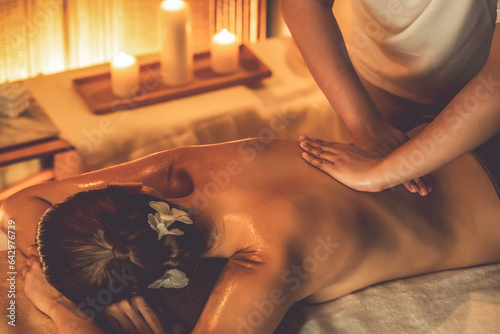 Caucasian woman customer enjoying relaxing anti-stress spa massage and pampering with beauty skin recreation leisure in warm candle lighting ambient salon spa at luxury resort or hotel. Quiescent