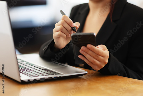 Businesswoman in working environment typing on a laptop and typing on smartphone with pen