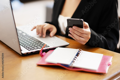 Businesswoman in working environment typing on a laptop and holding a smartphone