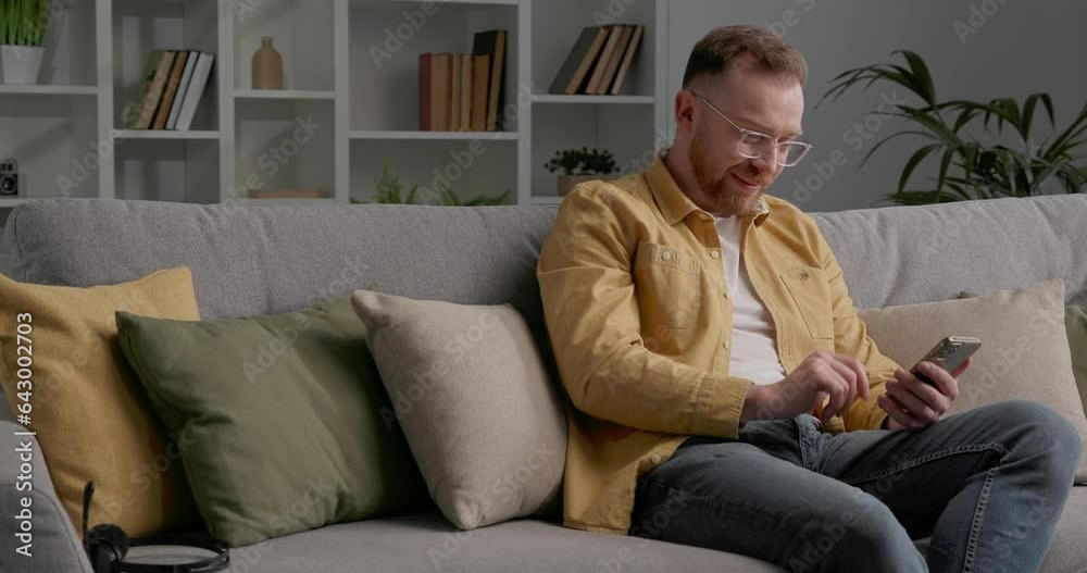 Casually dressed man sitting on cozy sofa while using smartphone. Casually dressed man sitting on cozy sofa while using smartphone.
