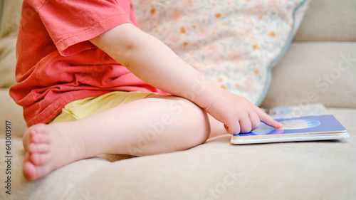 The cute baby is playing with the colorful picture book, flipping through the pages and touching the pictures. The little child reads book. Kid aged about two years (one year ten months)