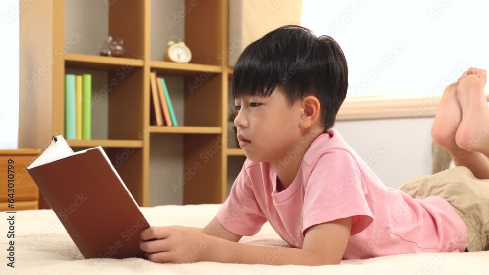 Asian handsome boy reading favorite book while lying down on bed at home, happy little kid spend time free to their advantage. Son enjoying reading manga new story. staying at home in self isolation. Asian handsome boy reading favorite book while lying down on bed at home, happy little kid spend time free to their advantage. Son enjoying reading manga new story. staying at home in self isolation.