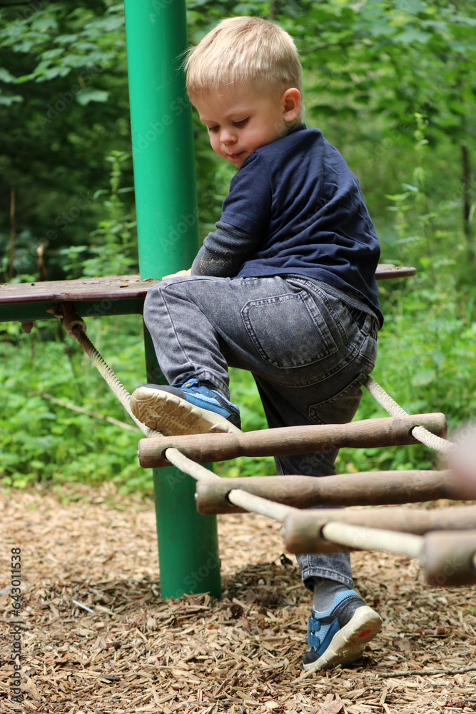 Little caucasian boy climbing and playing on a playground in the forest Little caucasian boy climbing and playing on a playground in the forest