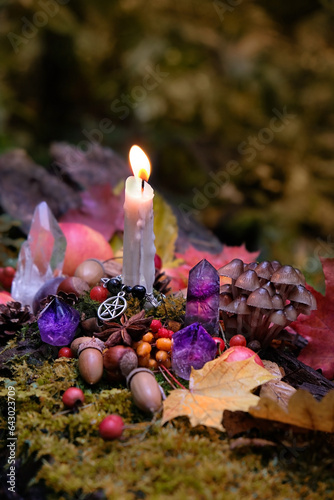 autumn background. Candle with amulet, crystals, fall leaves, fruits, berries, nuts in forest, natural backdrop. Wiccan altar for Mabon sabbat. autumn equinox. Witchcraft, magic, esoteric ritual