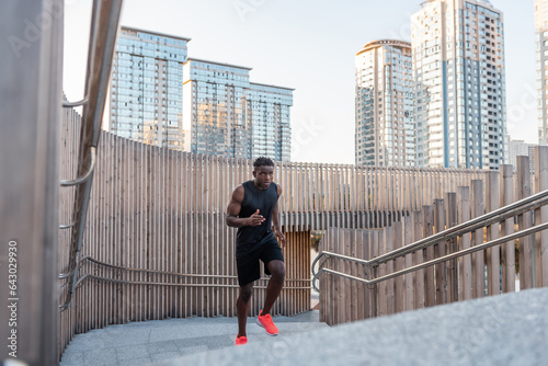 Handsome African man in sportswear looking concentrated while running up by stairway outdoors