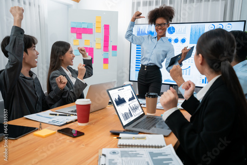 Business people celebrate after successful presentation or meeting on data analysis display on TV screen. Happy team gathers in office room, cheer to collaboration with celebratory gesture. Concord