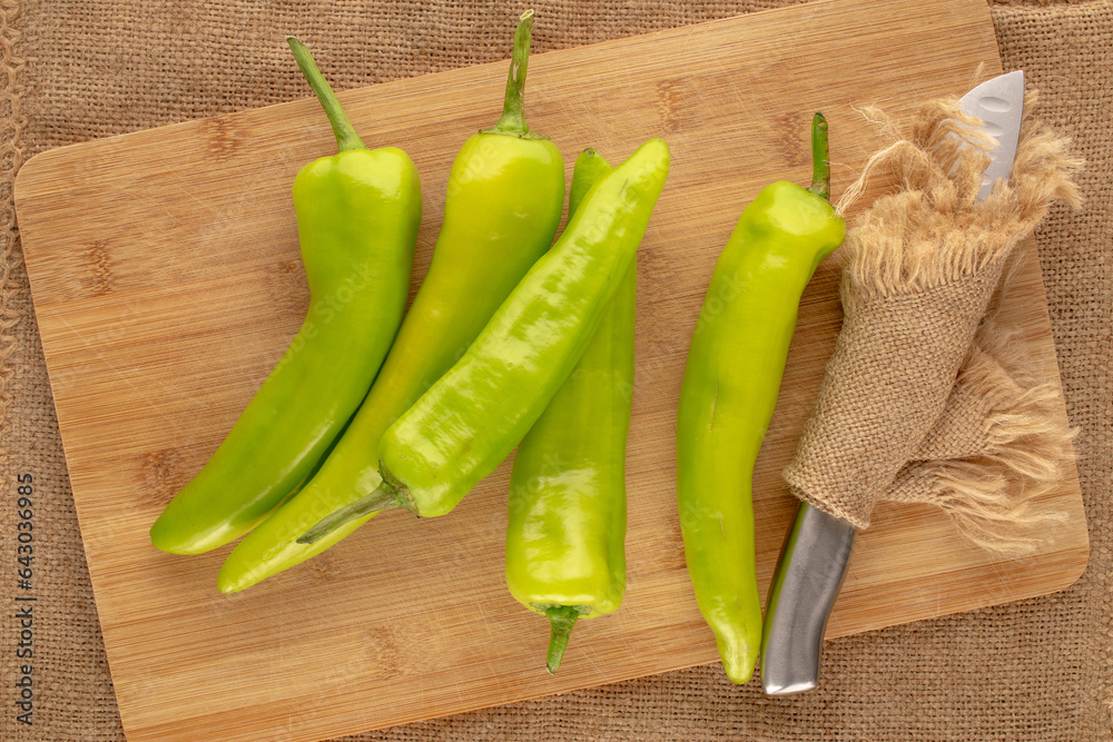 Several green chili peppers with wooden kitchen board and metal knife on jute cloth, macro, top view. Several green chili peppers with wooden kitchen board and metal knife on jute cloth, macro, top view.