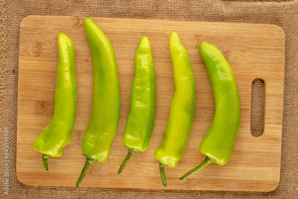 Several green chili peppers with wooden kitchen board on jute cloth, macro, top view. Several green chili peppers with wooden kitchen board on jute cloth, macro, top view.