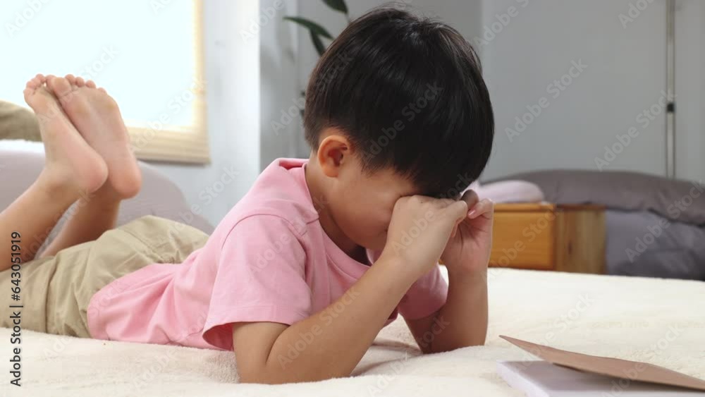 Asian little child boy feeling sleepy yawn and rubbing both eyes with
