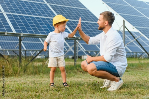 A father and his little son near the solar panels. A little boy in a yellow helmet