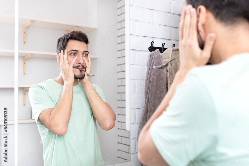 Handsome man doing facial workout with spoon exercises in front of the mirror. Young guy holding spoon with mouth Handsome man doing facial workout with spoon exercises in front of the mirror. Young guy holding spoon with mouth